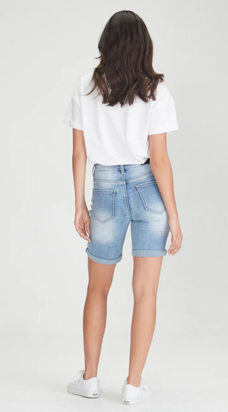 Rear view of a woman wearing a white t-shirt, light blue denim shorts, and white sneakers.