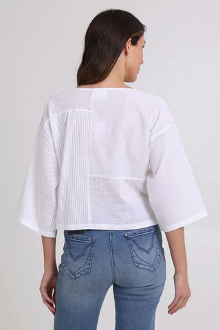 Rear view of a woman wearing a white textured mixed-fabric top and blue jeans.