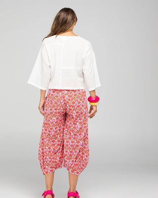 Woman from behind wearing a white short-sleeved top and red patterned wide-leg pants.