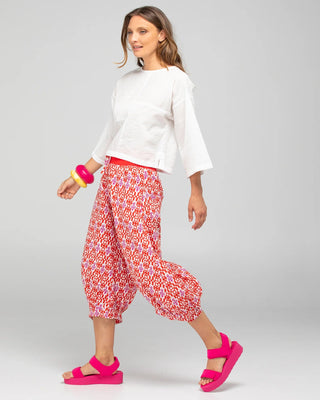 Woman wearing a white short-sleeved top, red patterned harem pants, and pink platform sandals.