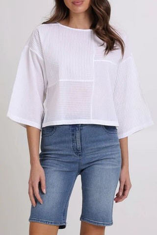 Woman wearing a white mixed-texture short sleeve top and blue denim shorts.