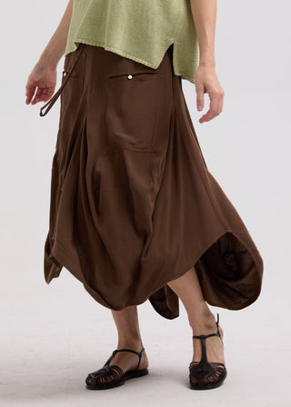 Woman wearing a brown midi skirt, light green top, and brown strappy sandals.