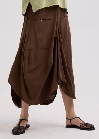 Woman wearing a long brown asymmetric skirt and black strappy sandals.