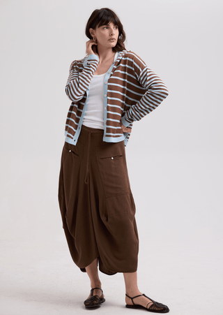 Woman wearing a brown and blue striped cardigan over a white top and brown wide-leg trousers.
