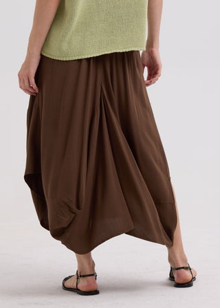 Woman wearing a pale green knit top and a brown draped midi skirt with black sandals