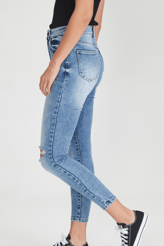 Woman wearing light wash blue ripped skinny jeans and black sneakers.
