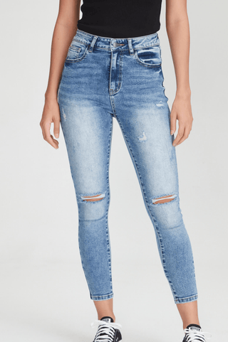 Woman wearing blue distressed skinny jeans with knee rips and a black top.