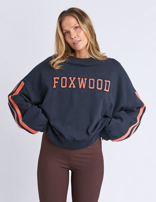 Woman wearing a navy Foxwood sweatshirt with orange lettering and stripe details.
