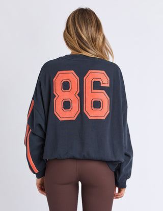 Back view of a woman wearing a navy oversized sweatshirt with large orange number 86 graphic.