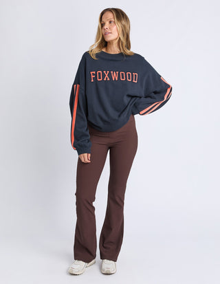 Woman wearing a Foxwood navy sweatshirt with orange stripes and brown flare pants.