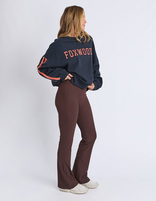 Woman wearing a navy Foxwood sweatshirt and brown flared leisure pants.