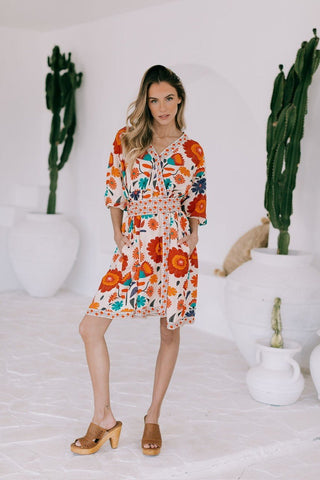 Woman wearing a colorful floral print short dress with puff sleeves and tan wedge sandals.