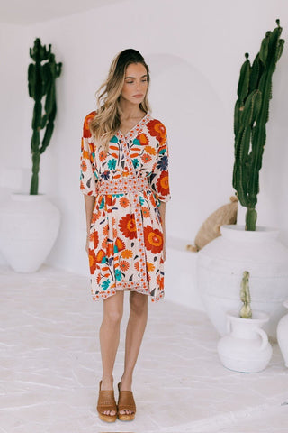 Woman wearing a colorful floral print wrap mini dress with long sleeves.