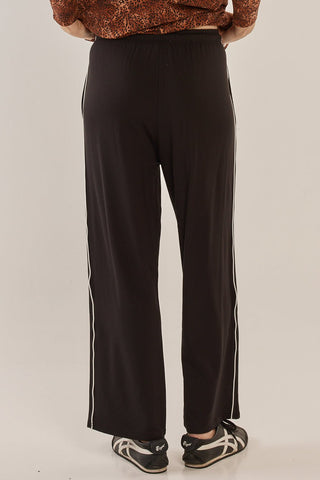 Rear view of a woman wearing black wide-leg leisure pants with white side stripes.