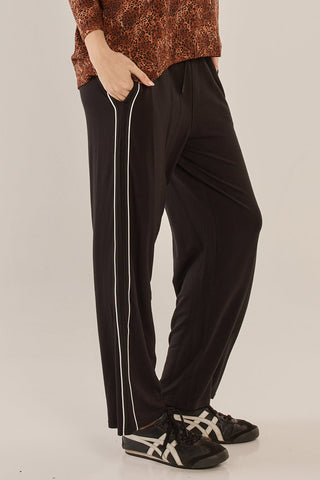 Woman wearing black wide-leg leisure pants with a white side stripe and sneakers.