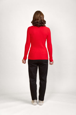 Woman wearing a red ribbed long sleeve top and black track pants with side stripes.