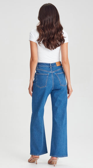 Woman wearing a white t-shirt and blue wide-leg denim jeans from a back view.