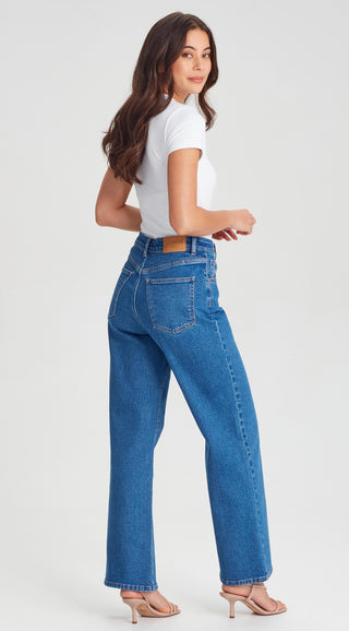 Woman wearing a white t-shirt and blue wide-leg denim jeans with beige heeled sandals.