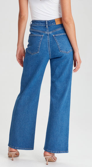 Woman wearing blue high-waisted wide leg denim jeans and white top.