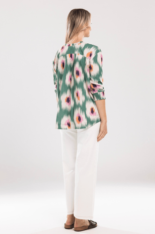 Woman wearing a green ikat print long sleeve blouse and white linen pants.