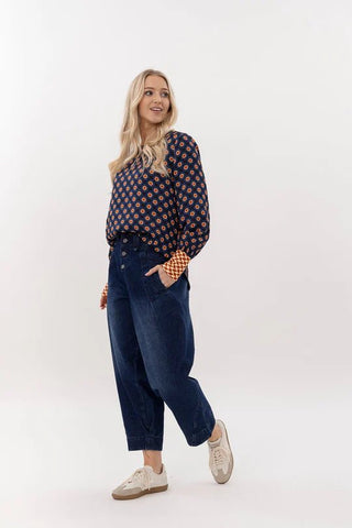 Woman wearing a navy blue patterned blouse and dark wash wide-leg denim pants.