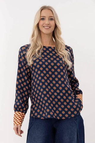 Woman wearing a navy blue patterned long sleeve blouse with orange geometric print.
