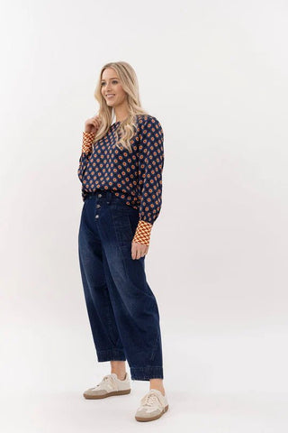 Woman wearing a navy patterned long sleeve blouse and wide leg dark denim jeans.