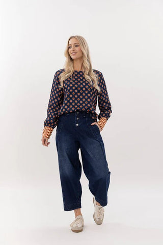 Woman wearing a patterned navy long sleeve blouse and dark denim wide leg pants.