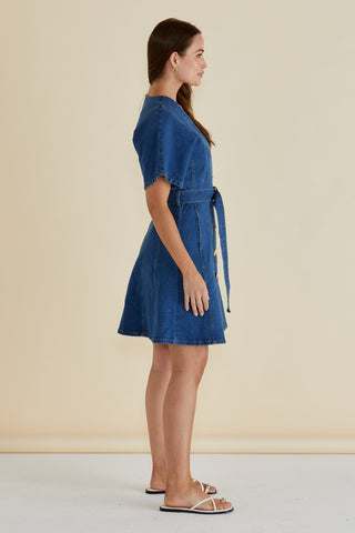 Side view of a woman wearing a short sleeve denim dress with a tie waist belt.