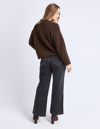 Woman wearing a brown oversized knit sweater and dark grey wide-leg jeans.