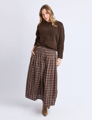 Woman wearing a brown textured sweater and a brown plaid maxi skirt with tan boots.