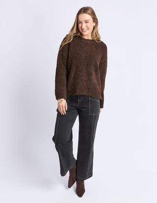 Woman wearing a brown textured knit sweater and black wide-leg pants with brown boots.