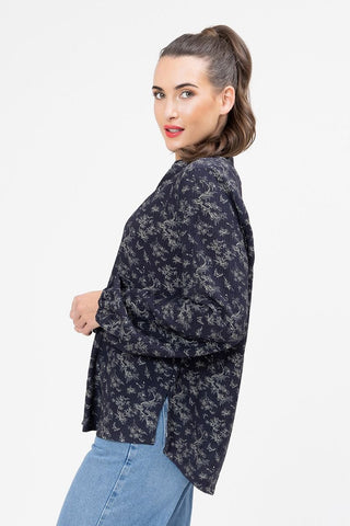 Woman wearing a black long-sleeve patterned blouse and blue denim skirt.