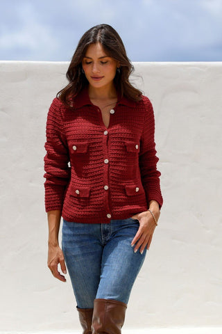 Woman wearing a red knit collared cardigan with gold buttons and blue jeans.