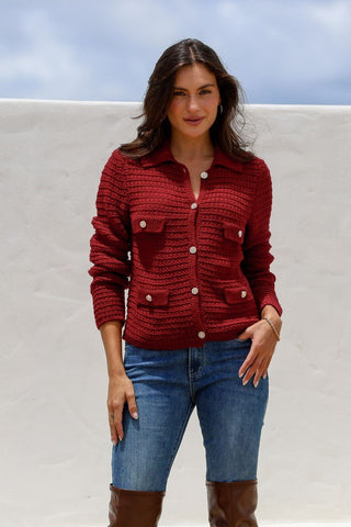 Woman wearing a red textured knit button-up cardigan and blue denim jeans.