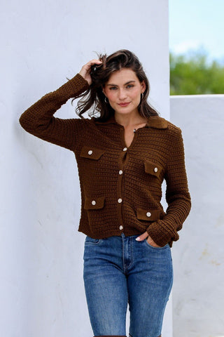 Woman wearing a brown textured knit button-up cardigan and blue denim jeans.