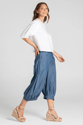 Woman wearing a white puff sleeve top and blue linen harem pants with wedge sandals.