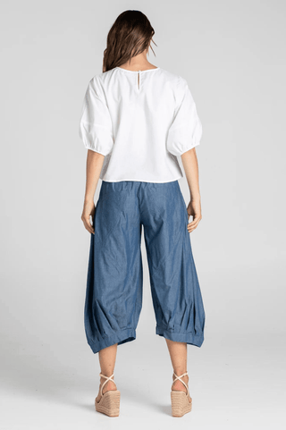 Woman wearing a white puff sleeve blouse and blue cropped wide-leg culotte pants.