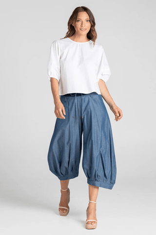 Woman wearing white puff sleeve blouse and blue denim balloon pants with wedge sandals.