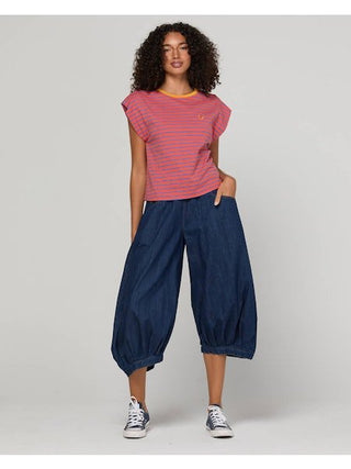 Woman wearing a pink striped t-shirt and navy blue denim balloon pants with sneakers.