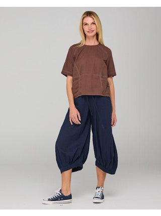 Woman wearing a brown short sleeve top and navy blue baggy harem pants with blue sneakers