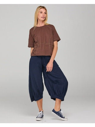 Woman wearing a brown short-sleeve t-shirt and navy blue harem style cropped pants.