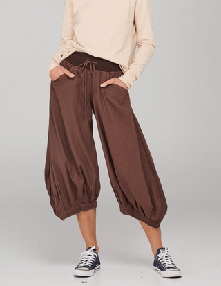 Woman wearing brown drawstring bubble pants, a beige long-sleeve top, and navy sneakers.