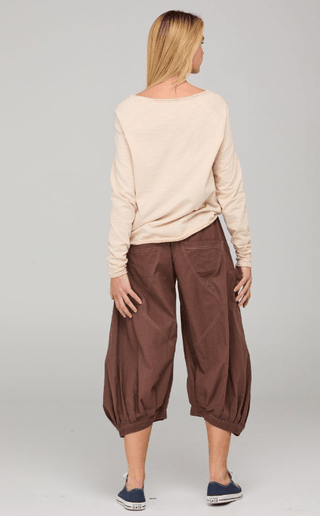 Rear view of a woman wearing a beige long-sleeved top and brown balloon-style pants.