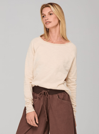 Woman wearing a cream long-sleeved sweatshirt and brown drawstring wide-leg pants.