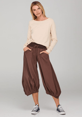 Woman wearing a cream long-sleeve top and brown balloon-style apartment pants.