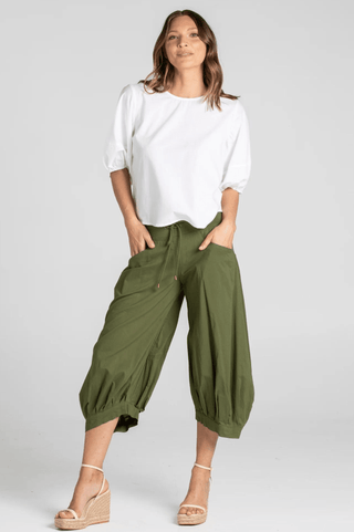 Woman wearing white puff sleeve blouse and olive green cropped harem pants with wedge sandals.