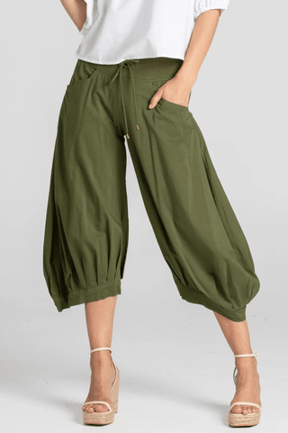 Woman wearing olive green cropped harem pants and white top with wedge sandals.
