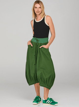 Woman wearing a black tank top and green balloon pants with green sneakers.