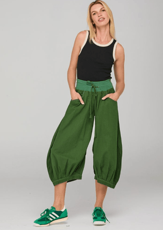 Woman wearing a black tank top, green harem pants, and green sneakers.